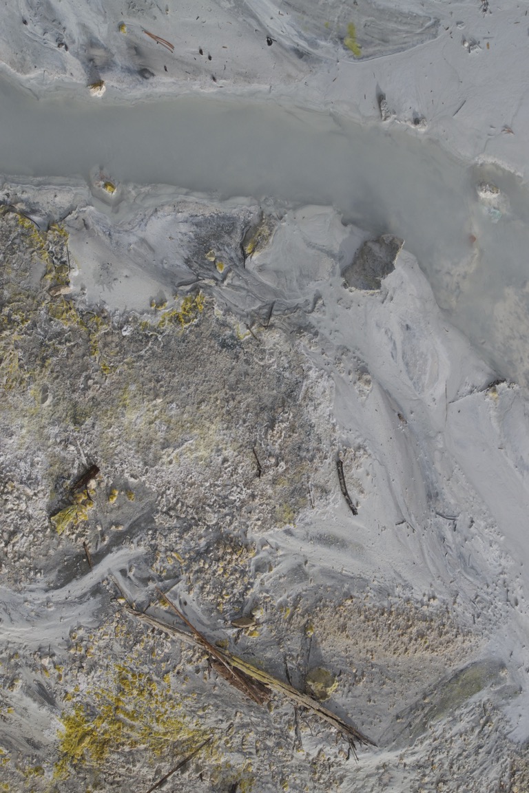 A closeup of the opaque gray water and yellow sulfur deposits.