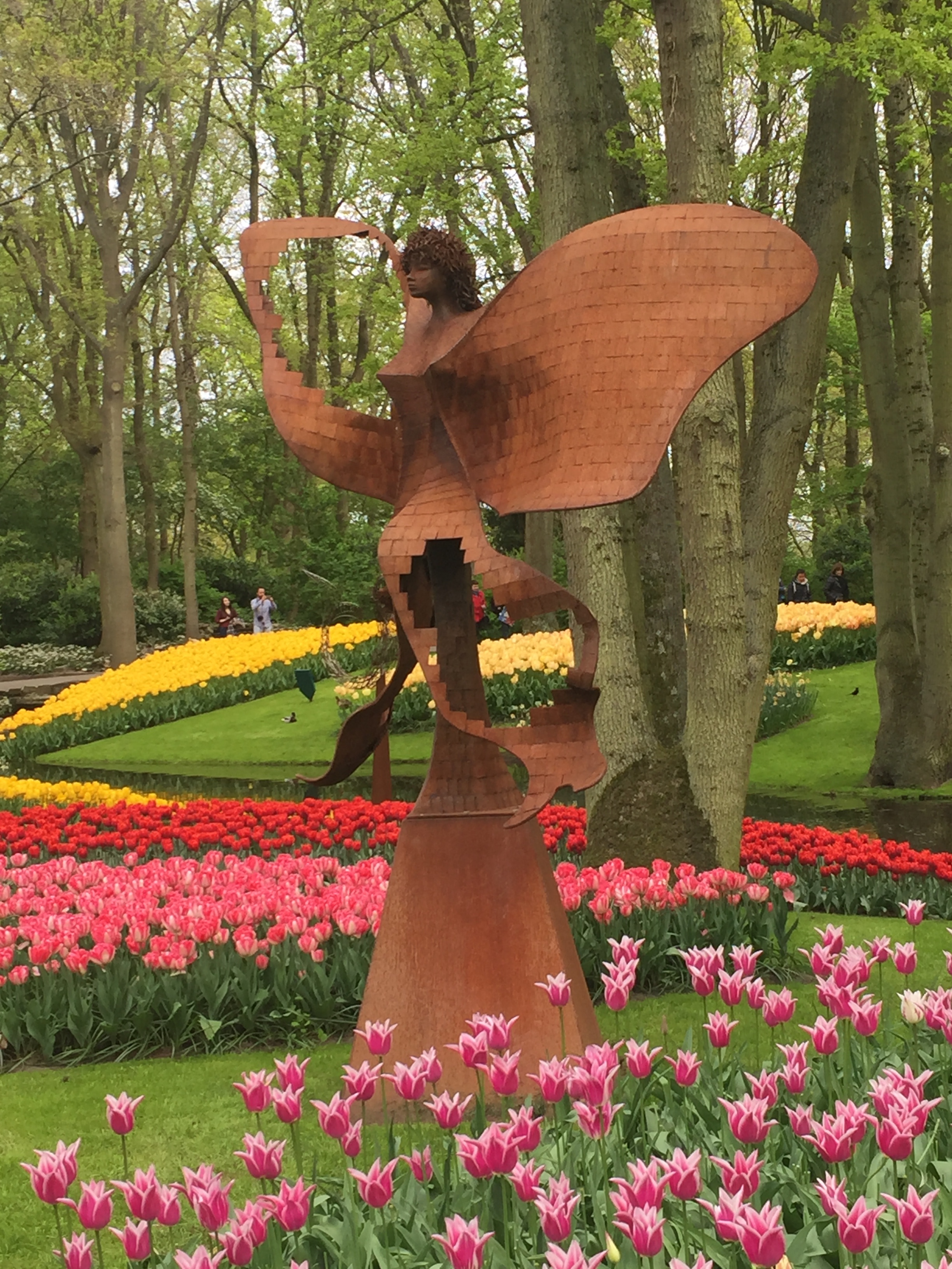 A bronze statue of a butterfly amidst beds of bright tulips.