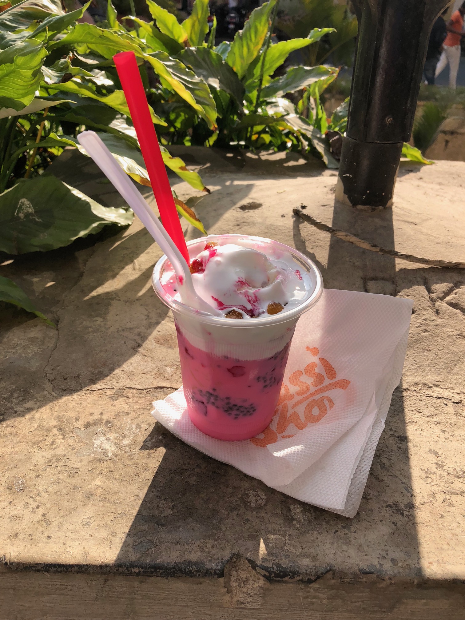 A straw and spoon stick out of a bright pink drink with ice cream on top.