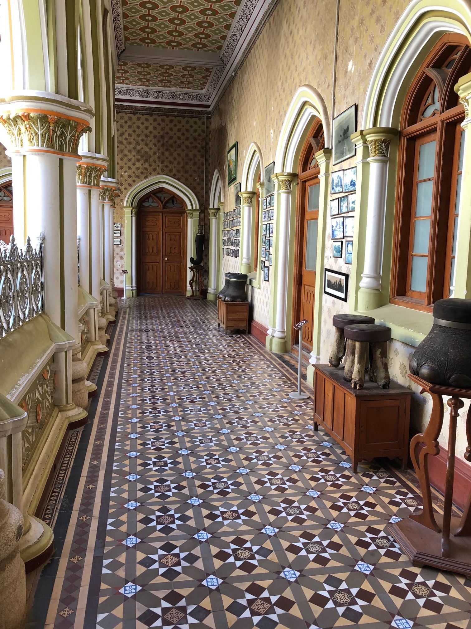 A mosaic-floored hall overlooks a square.  Stools made from the feet of  elephants and other animals sit on benches, on display.