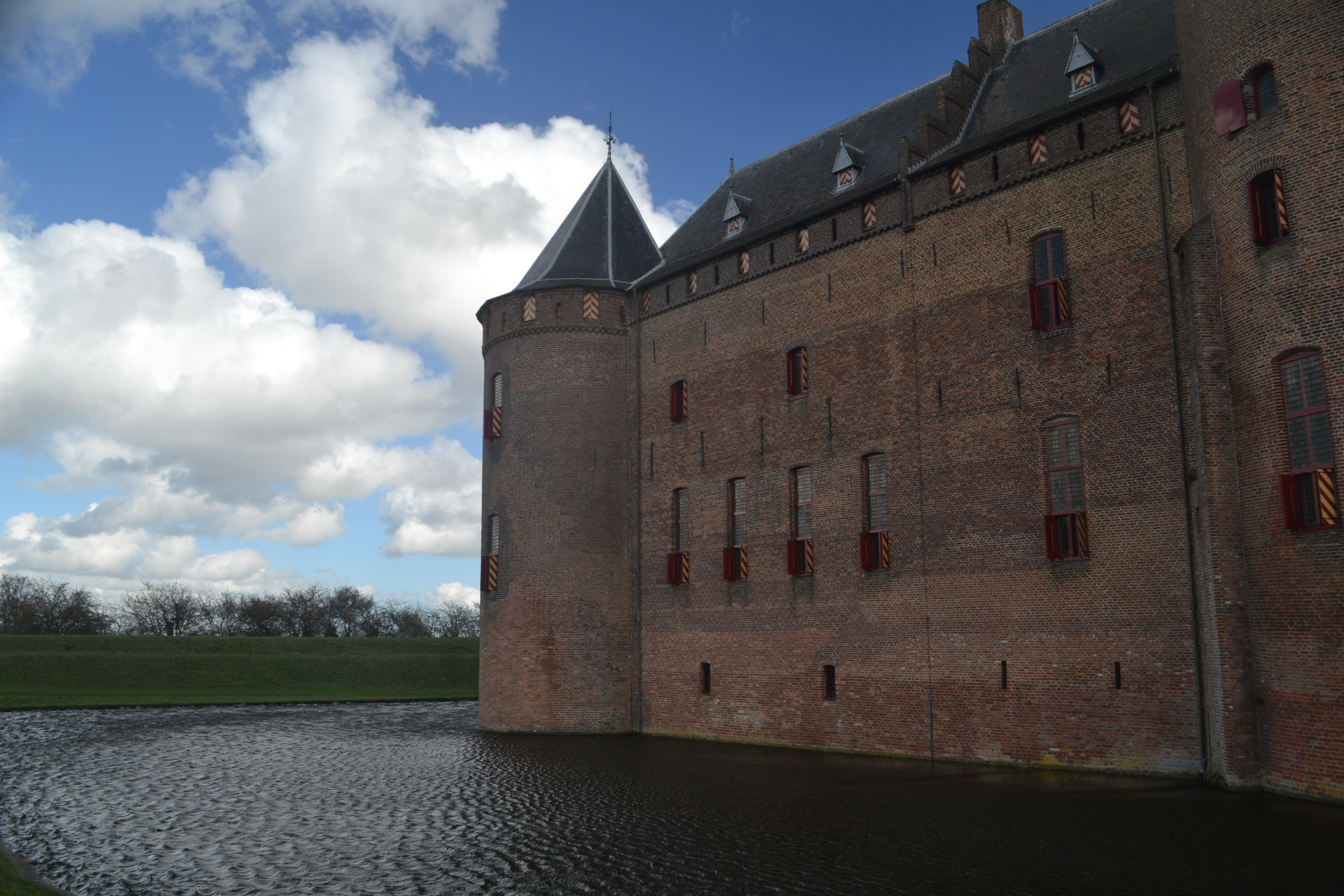 A castle of red bricks rises from a moat.  Red and yellow shutters decorate the windows.
