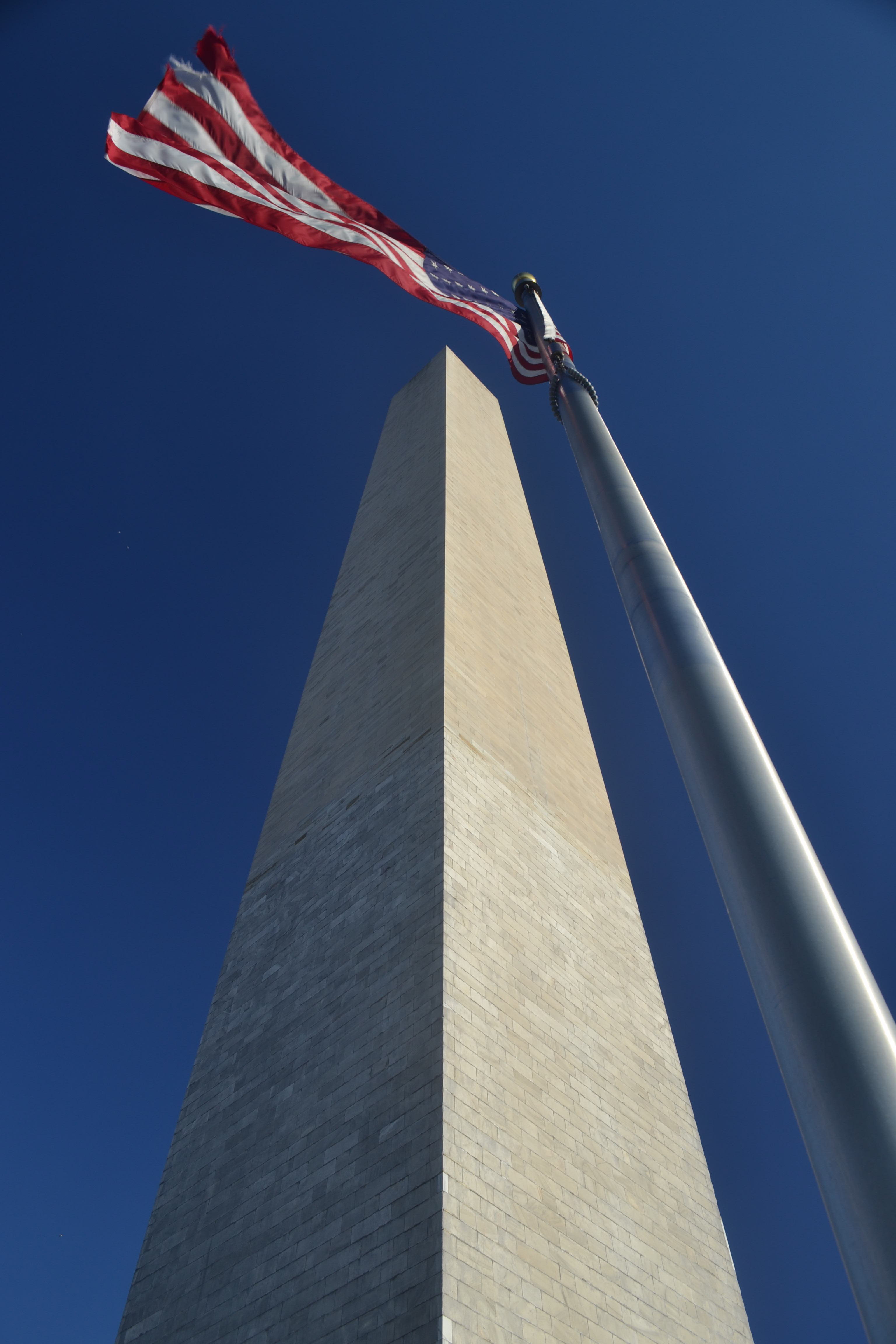 Looking up, a flag pole seems to parallel the Washington Monument so that an American flag flies above it.