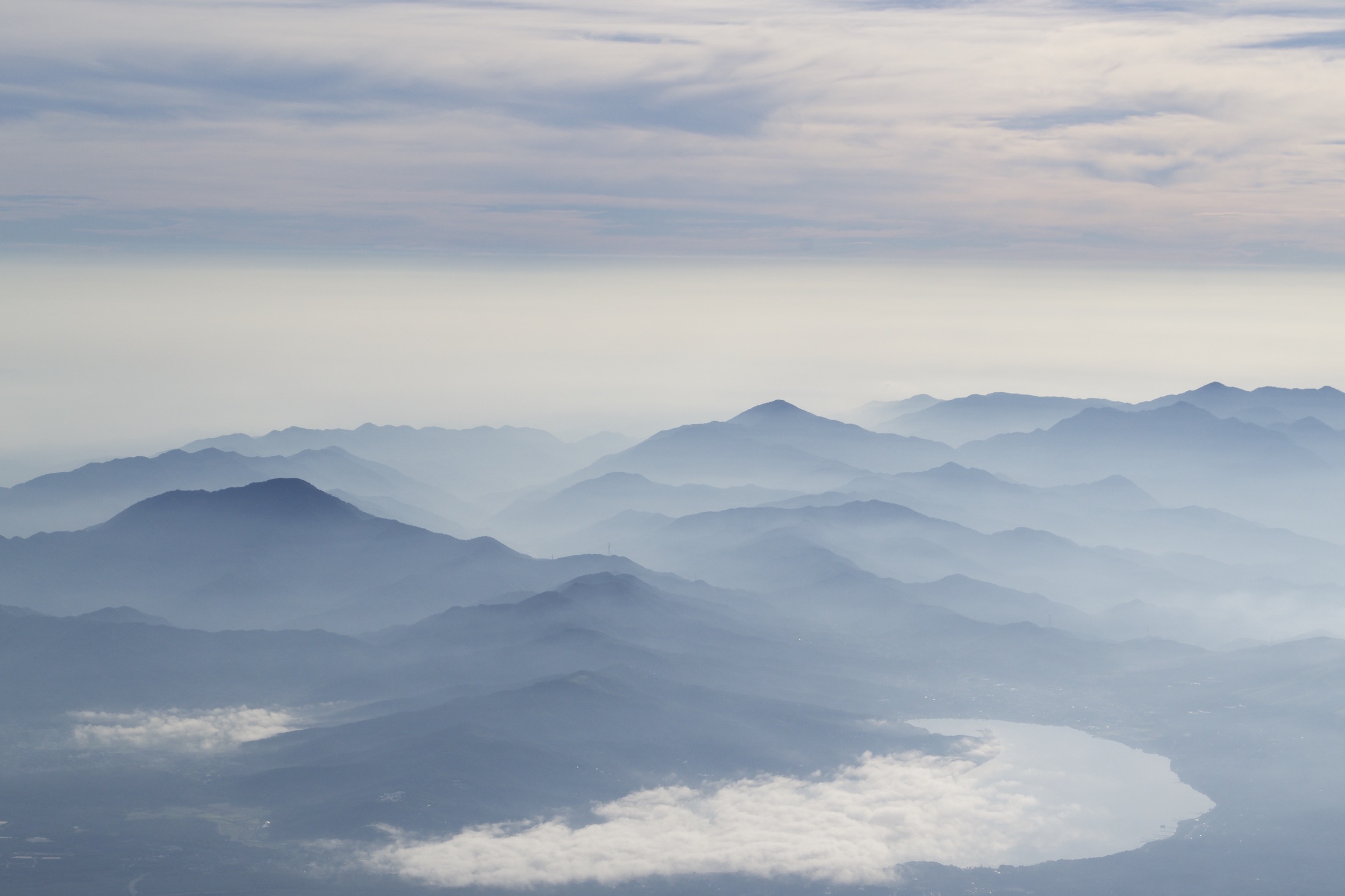 Silhouettes of mountains beneath a cloudy, pastel blue sky.