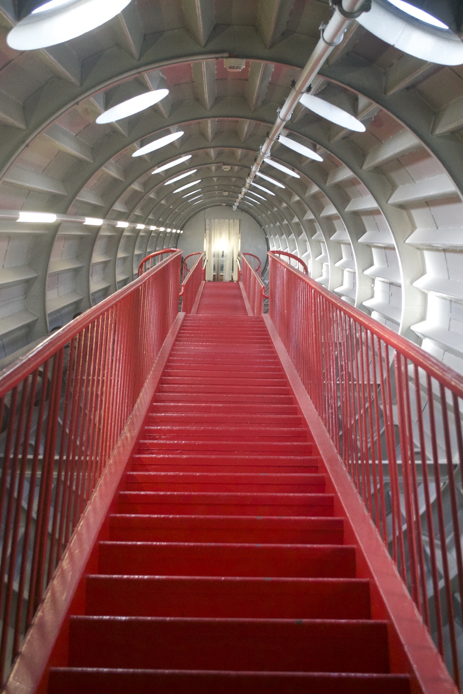 Two flights of red stairs go up a cylindrical tube.