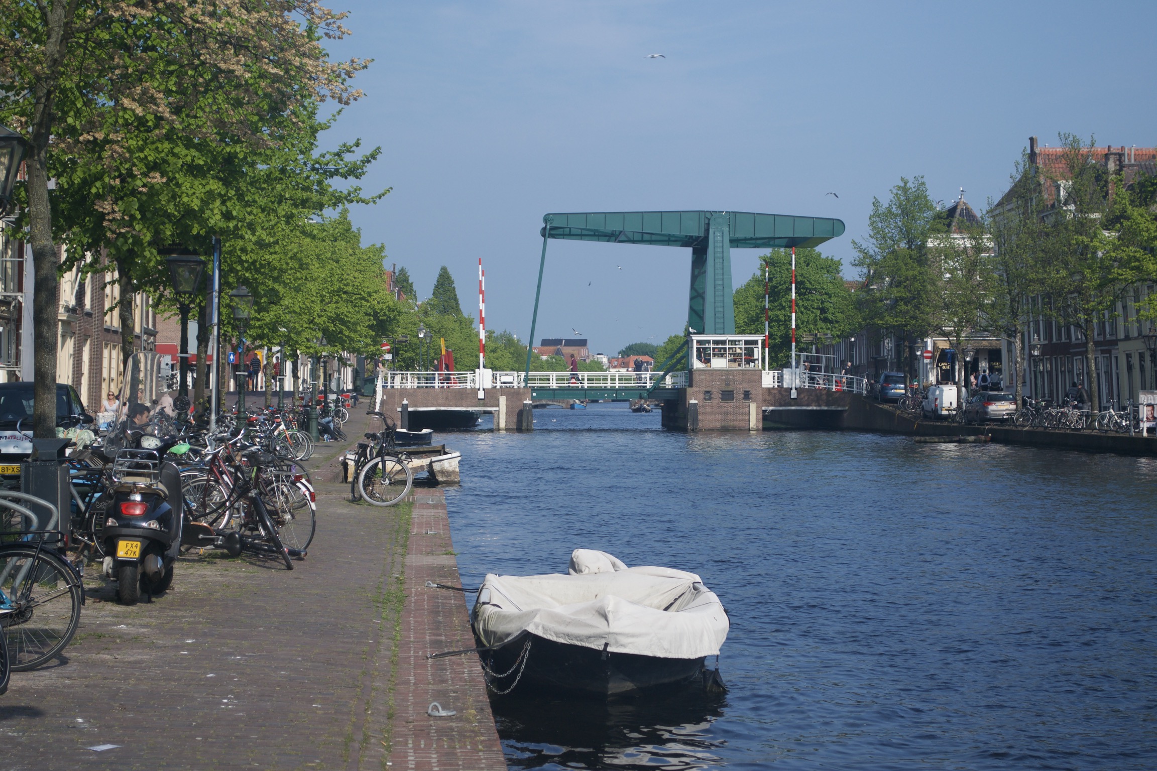 A boat tied up on the side of a canal, with a cantilevered drawbridge in the background.