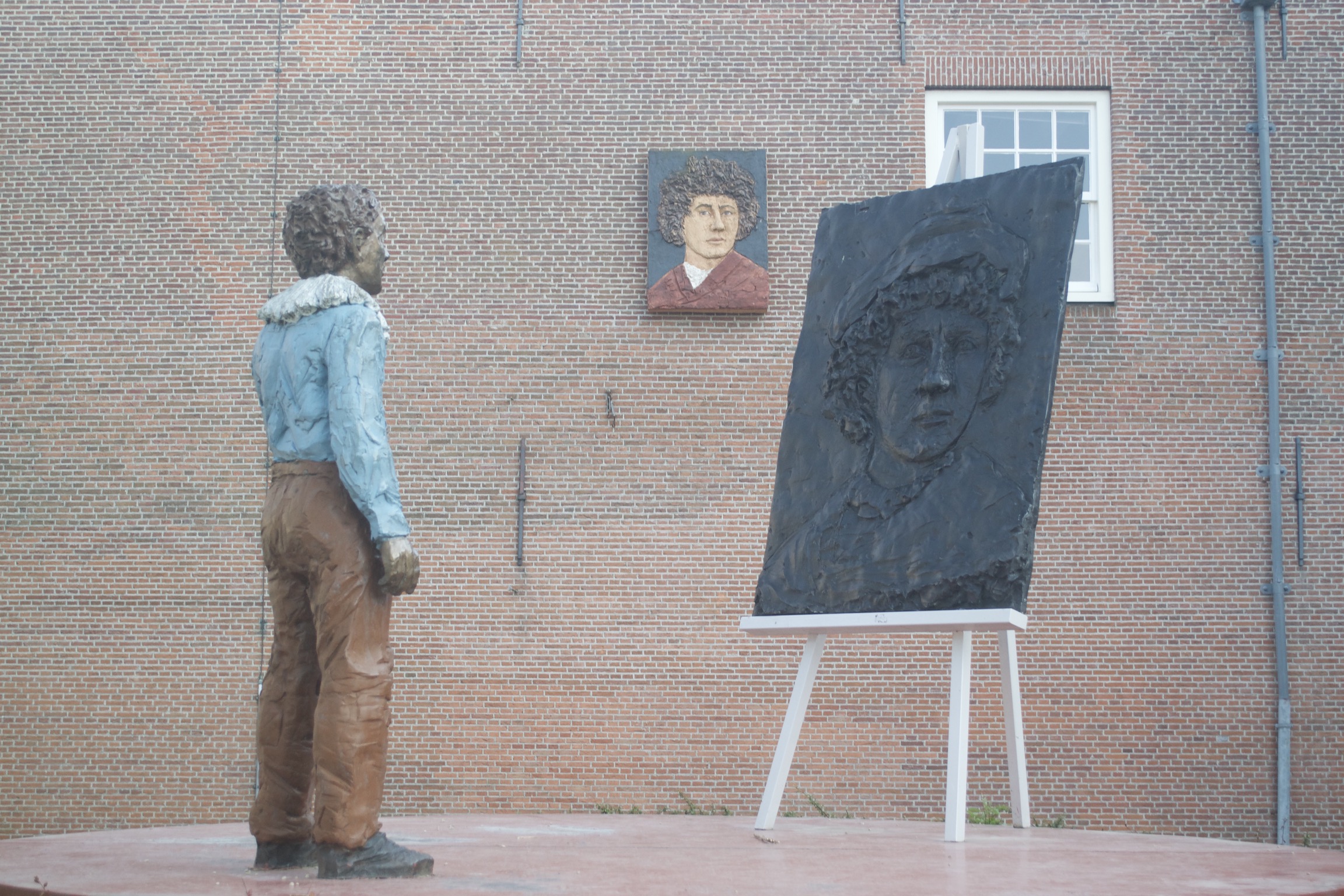 A statue of a man looking at a canvas with another man's face.  That same image hangs on a wall in the background.