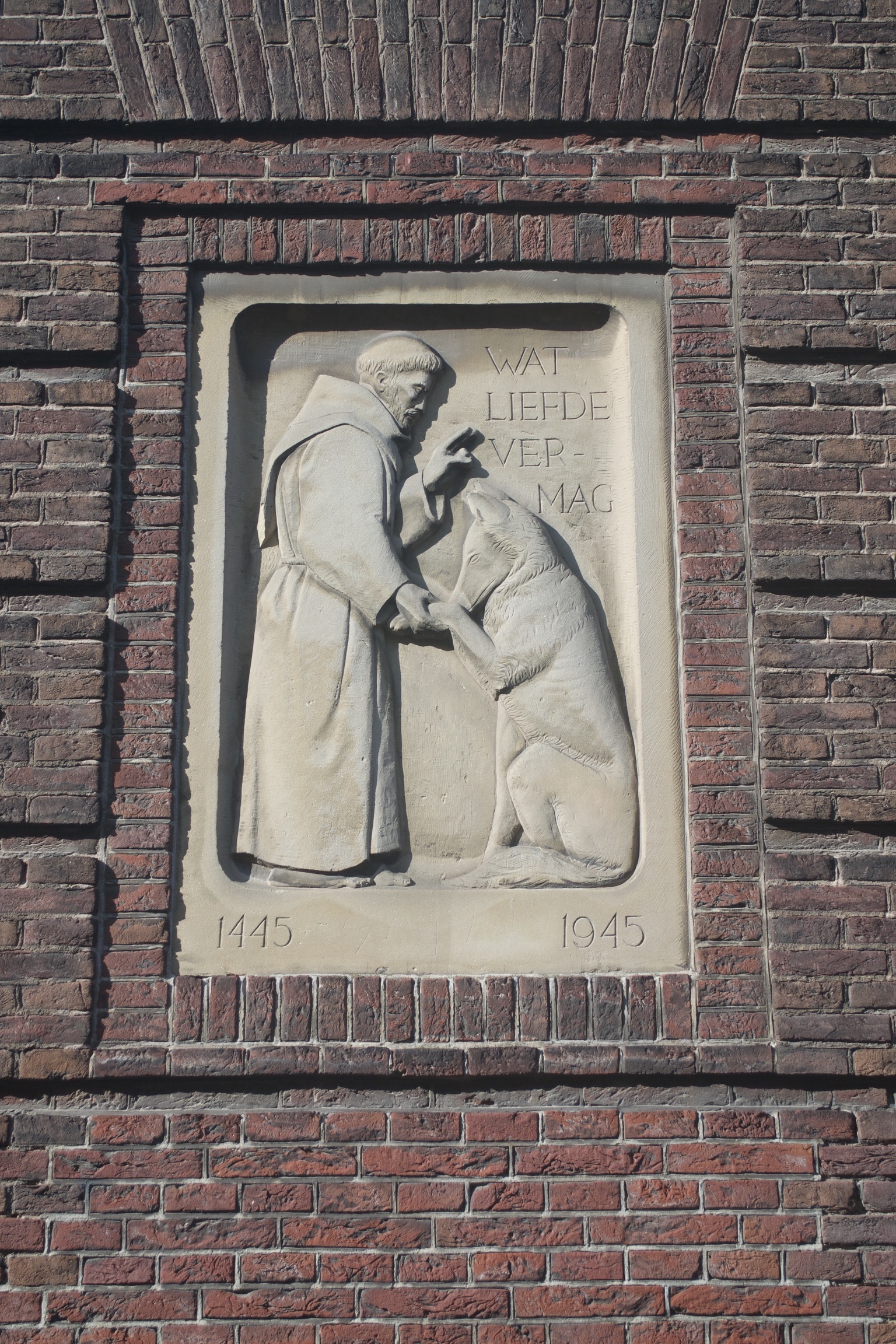 A carving of a monk blessing a dog, inscribed with the dates 1445 and 1945 in the bottom corners and 