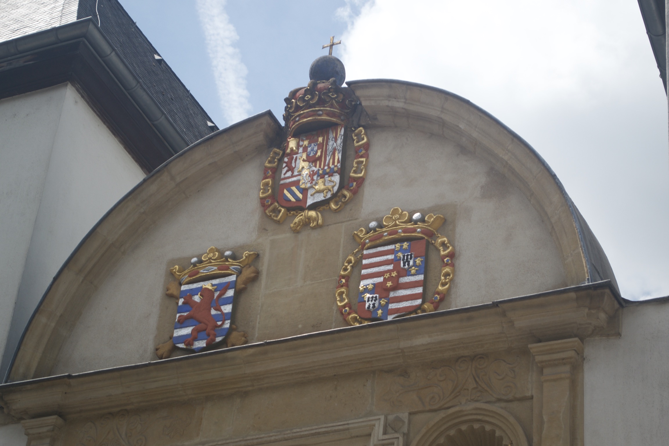 Three coats of arms, all red, yellow, and gold with lions, star, stripes, and crowns on a brown stone building.