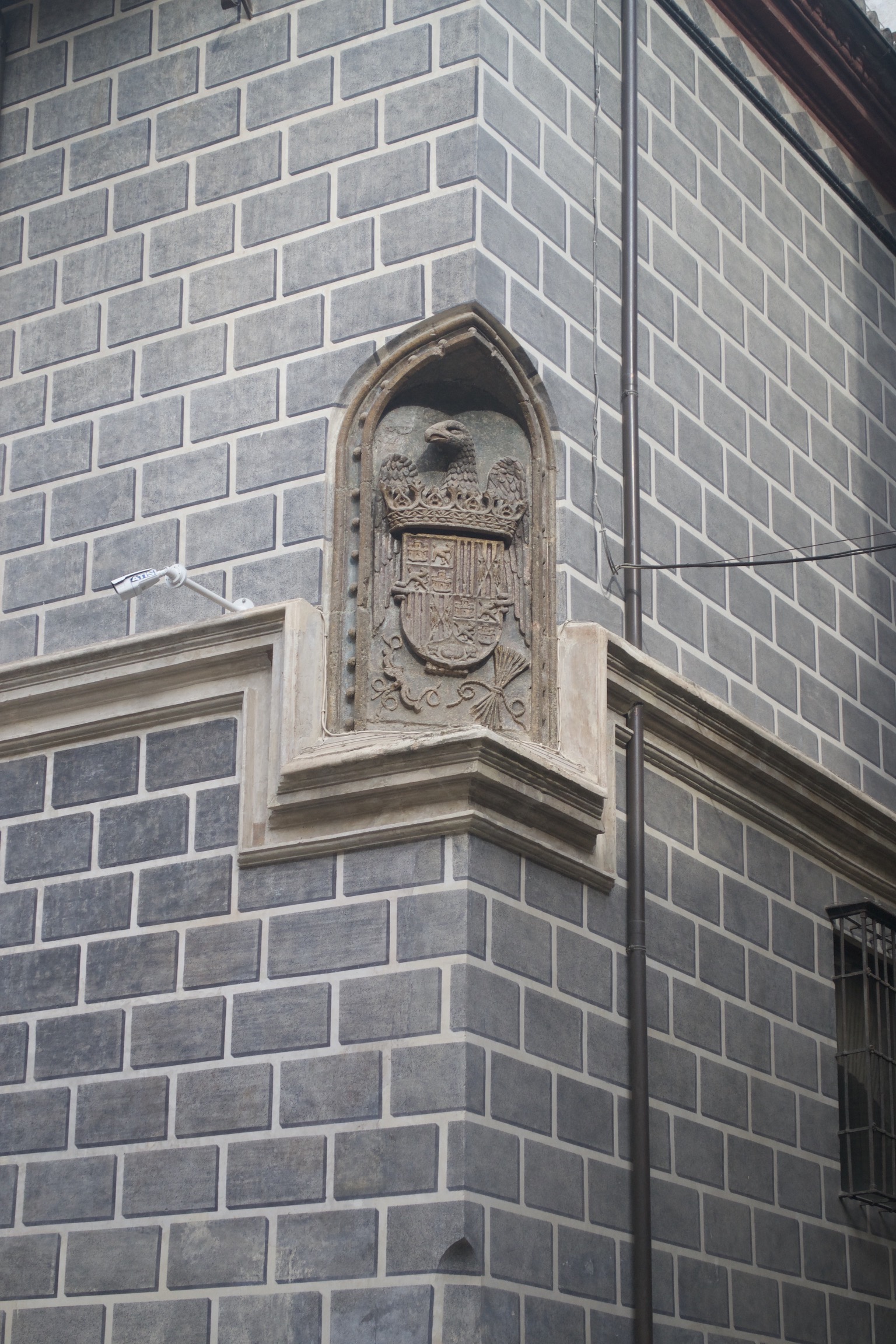 A coat of arms is built into the corner of a gray brick building.