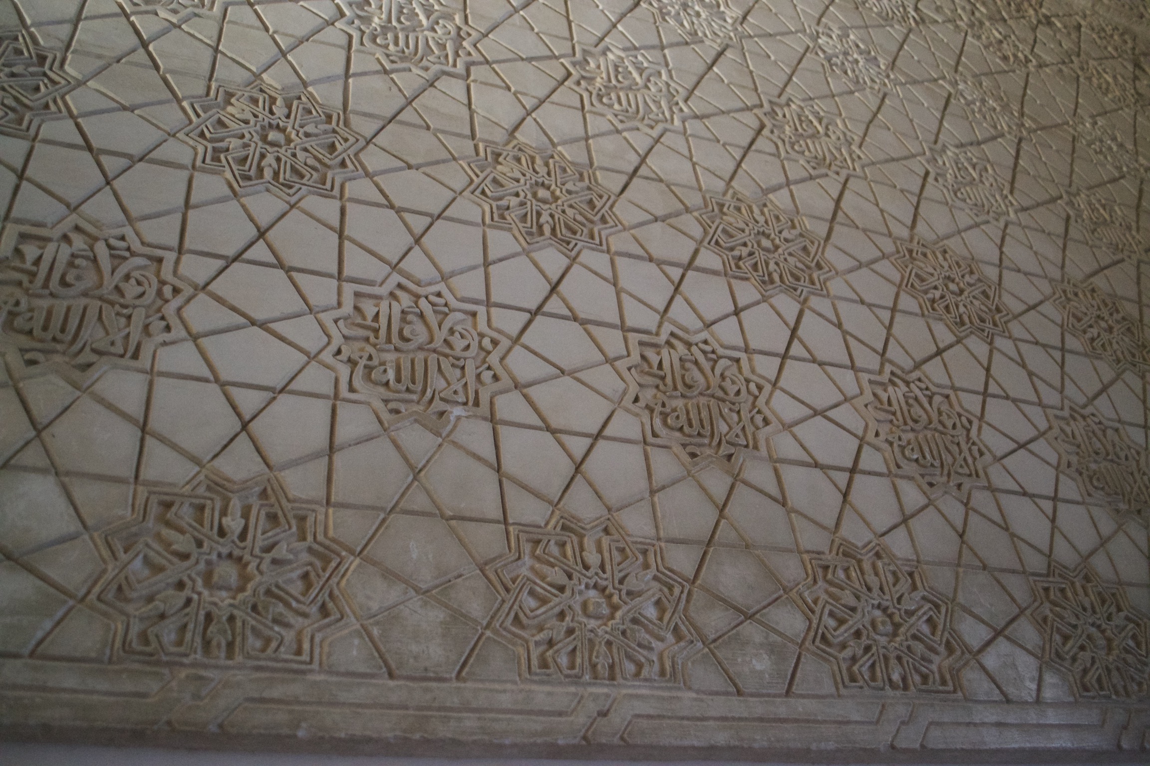 A tesselation of eight-pointed stars and rays emanating from them.  The stars' interiors contain either geometric designs or Arabic inscriptions.