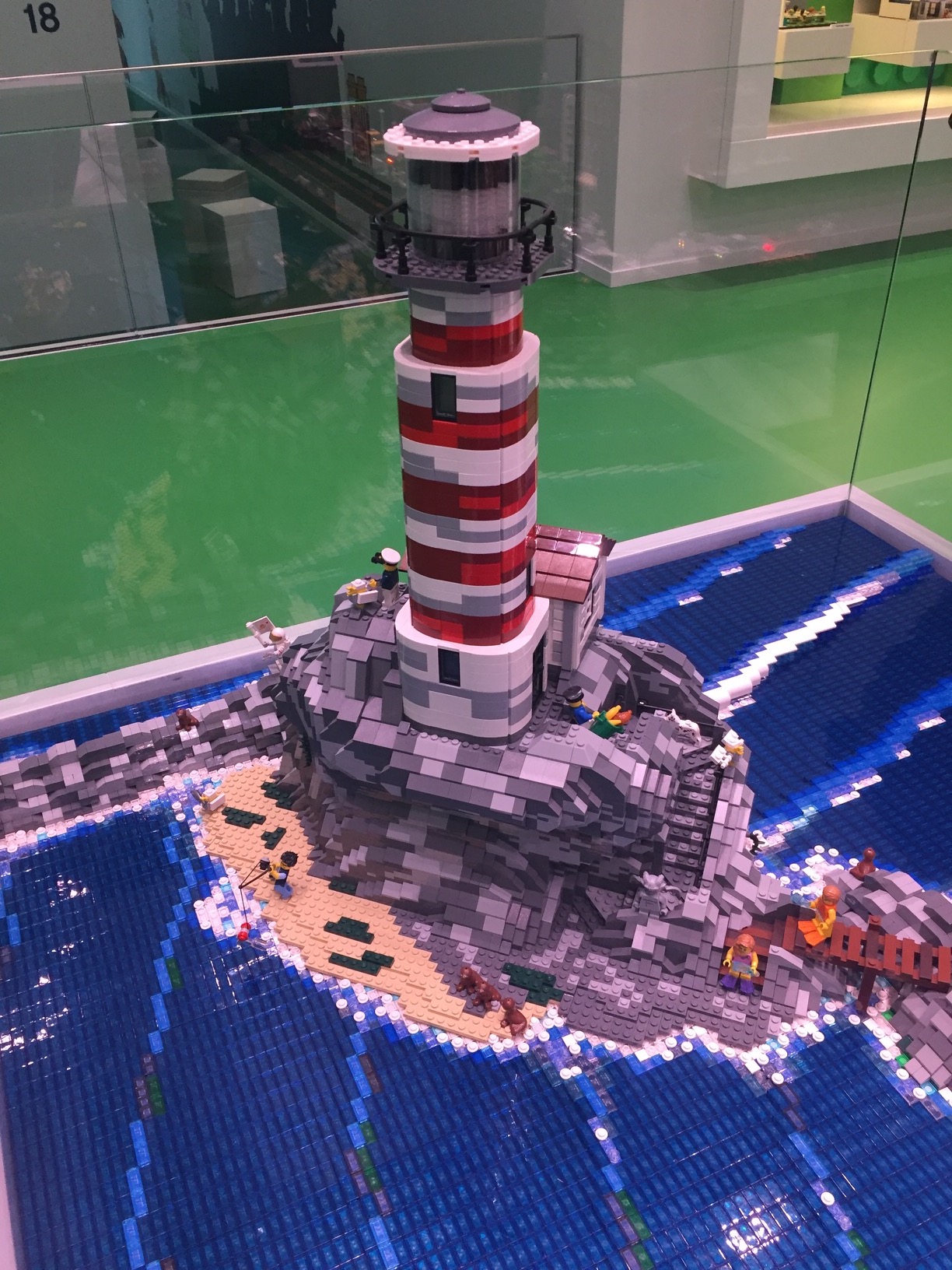 A LEGO lighthouse on a rocky island with a small beach, breaking the waves.