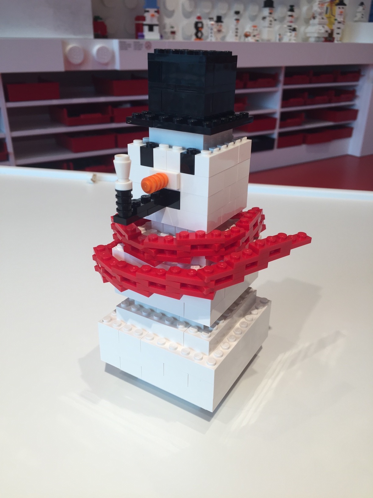 A blocky white LEGO snowman with a black tophat, orange nose, and red scarf smoking a black pipe.