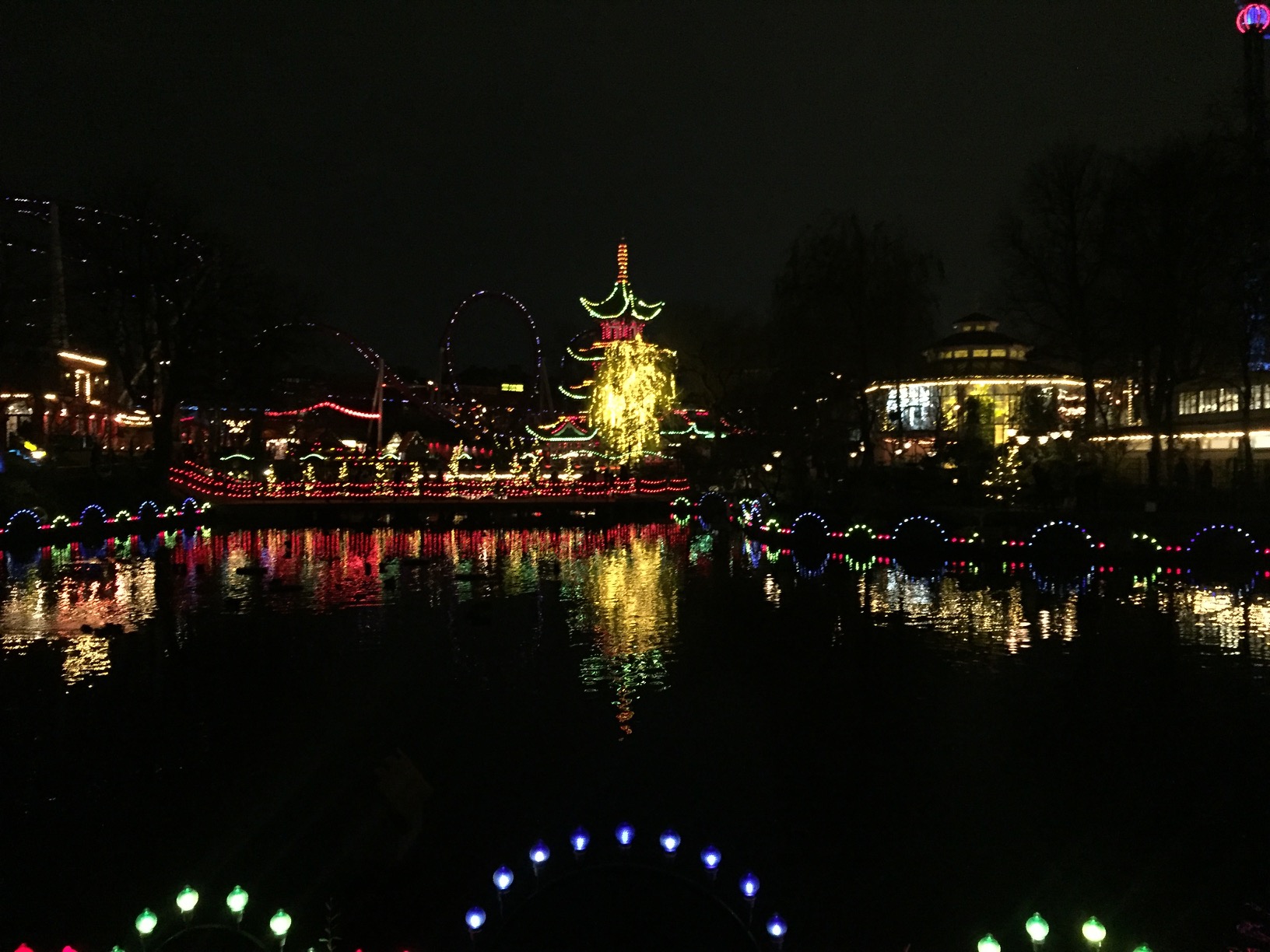 A lake reflects a lit-up amusement park pagoda.
