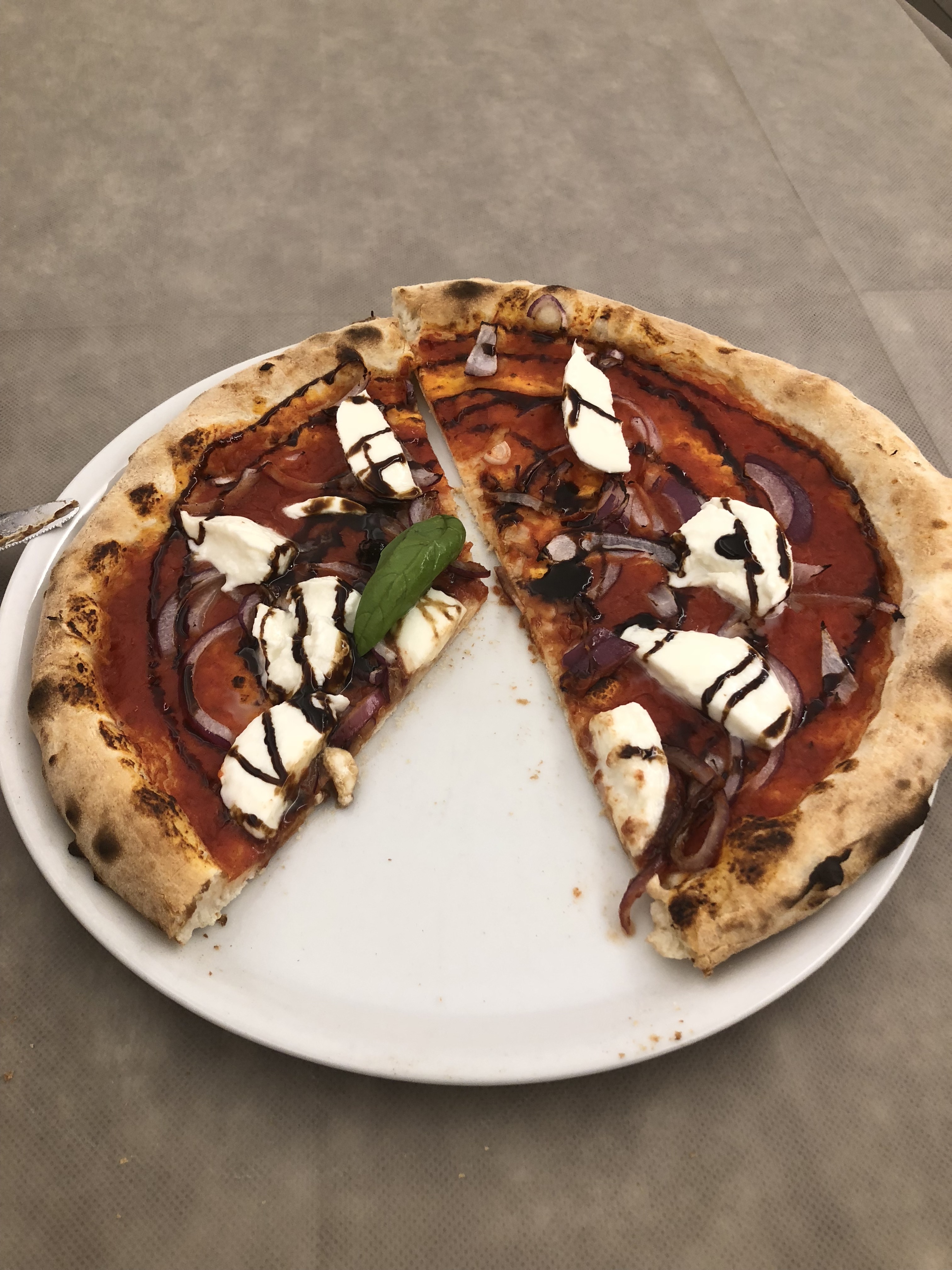 A pizza with fresh mozzarella drizzled with a reduced balsamic vinegar.  One slice is missing.