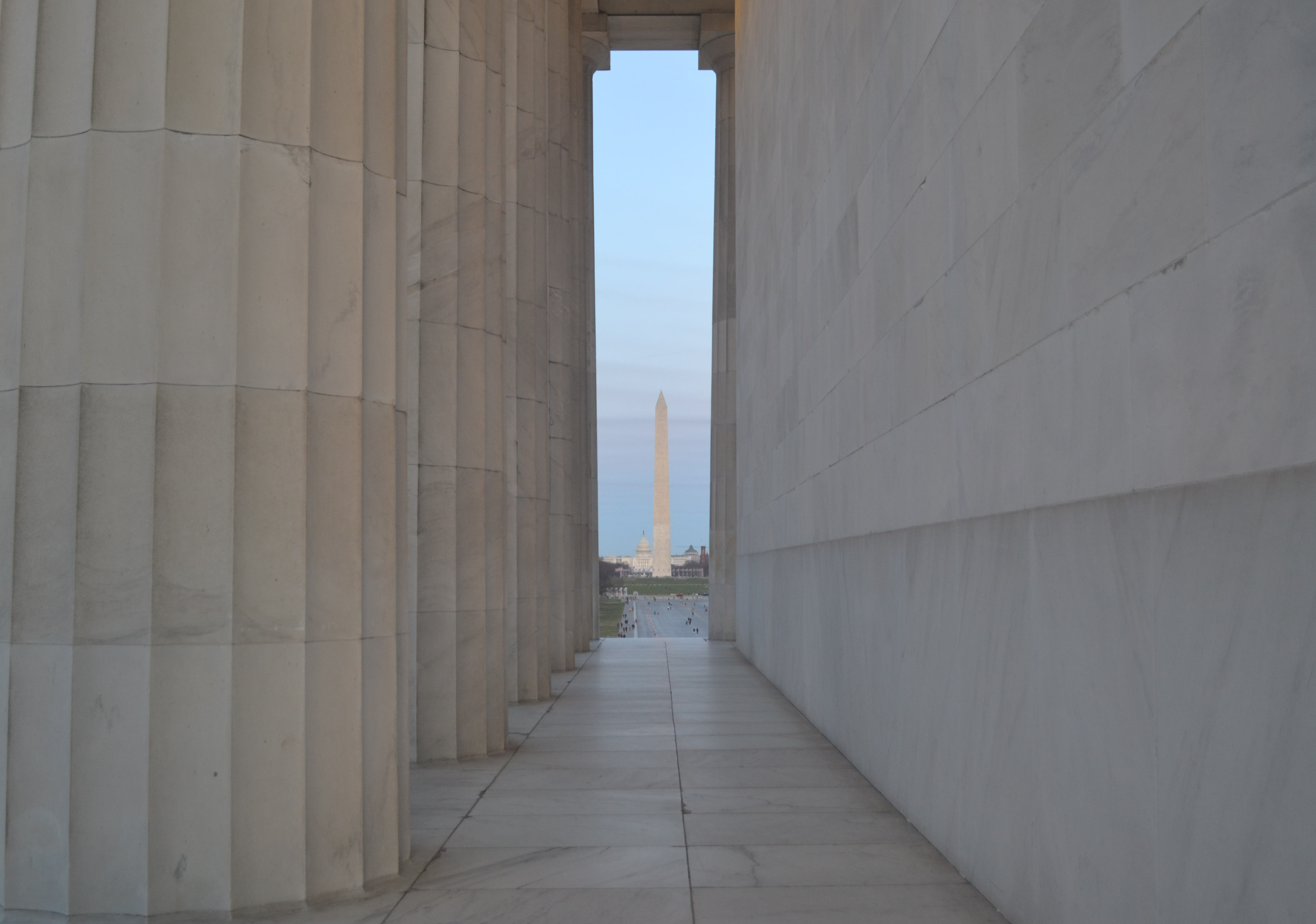 Ridged marble columns on the left, a flat marble wall on the right, and a polished marble floor, frame a distant obelisk and white dome.