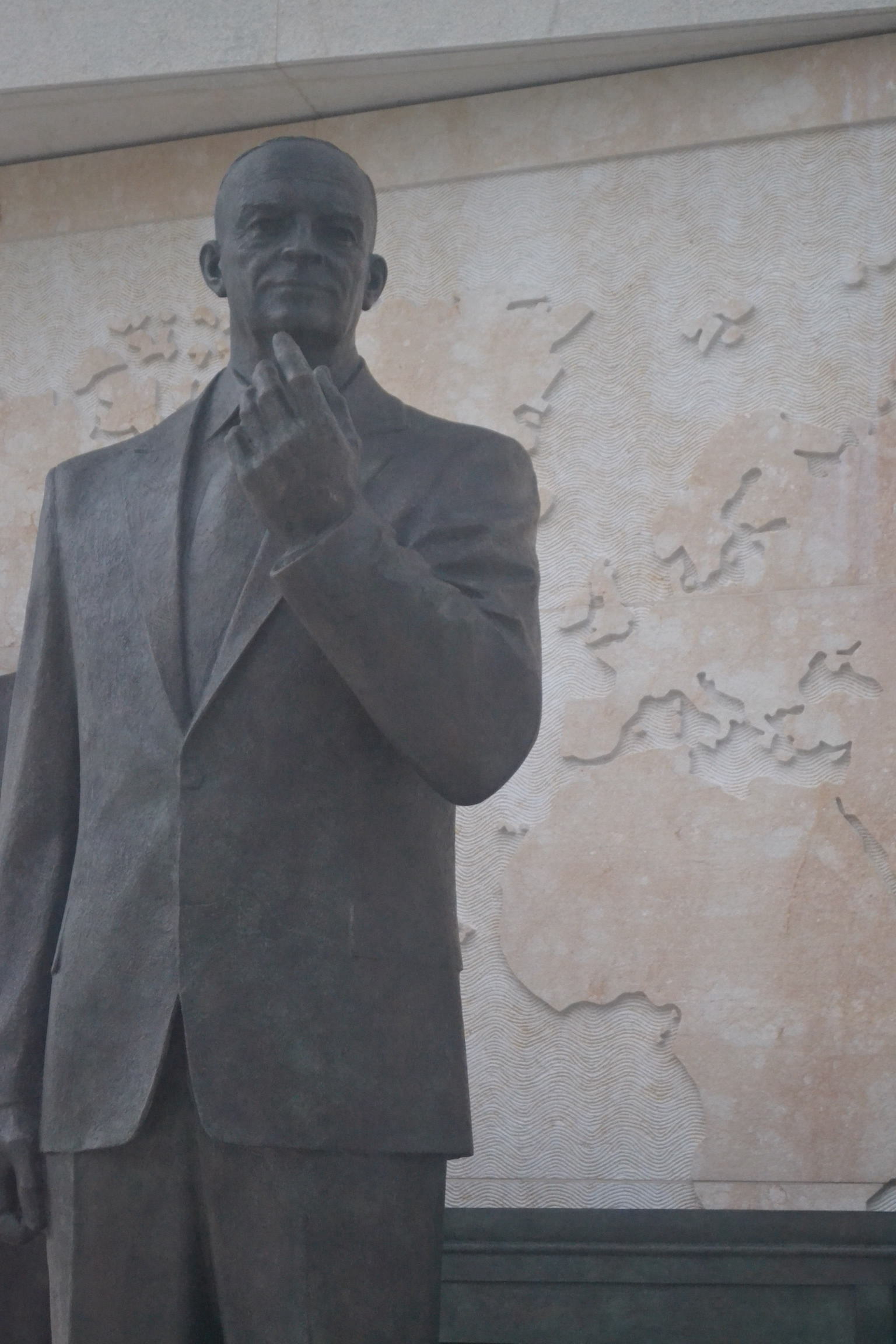 A bronze statue of a man in a suit before a piece of a world map.